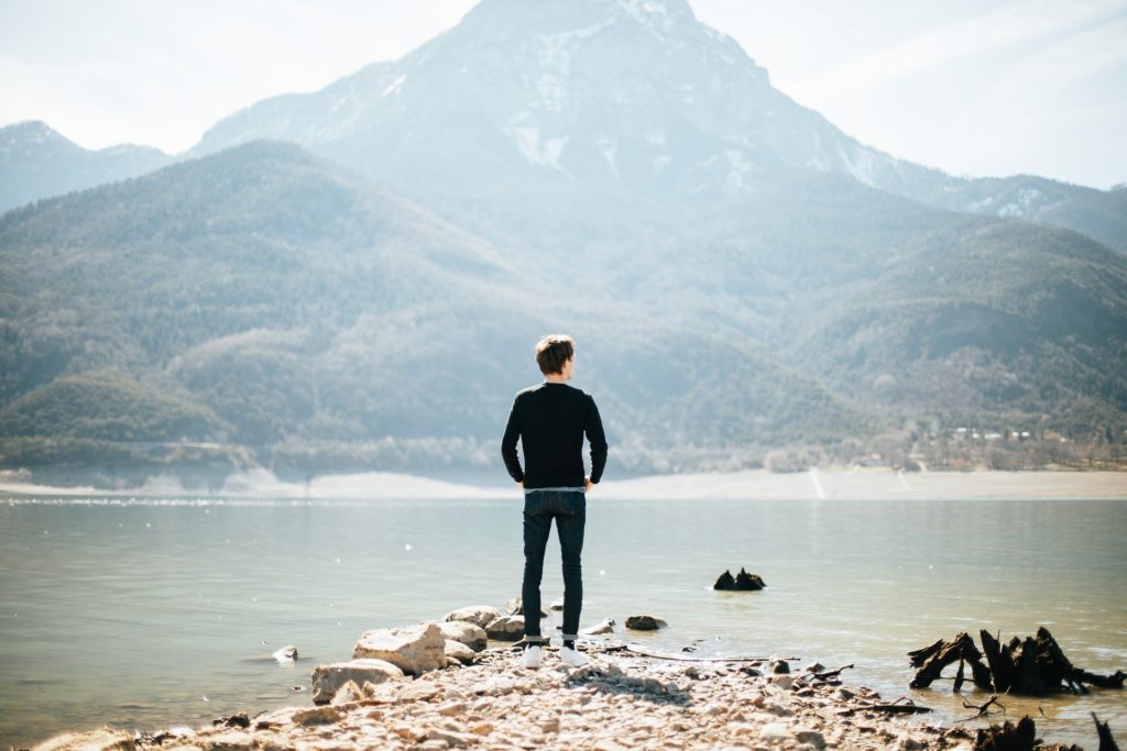 man looking across water at mountain