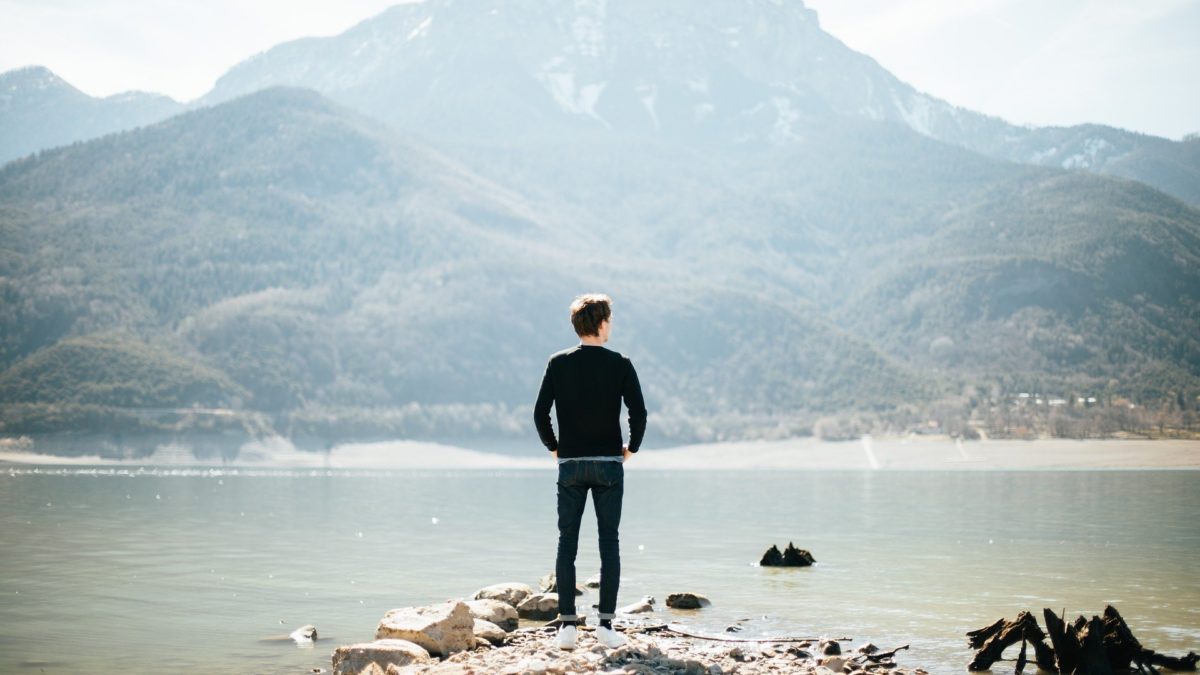 man looking across water at mountain