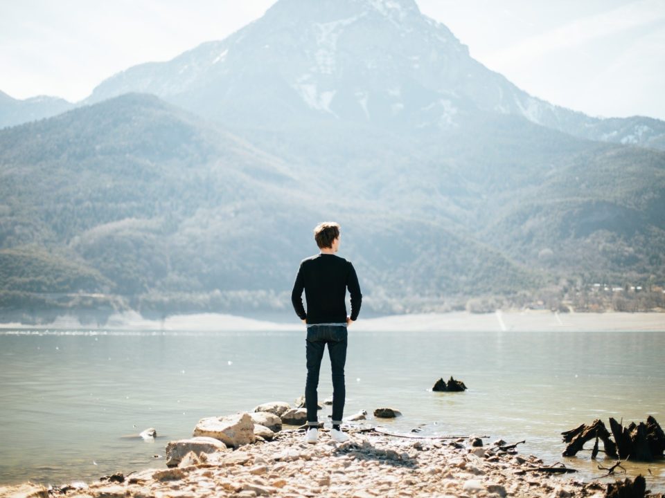man looking across water at mountain
